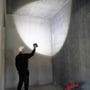 En håndværker retter lyset fra Scangrip NOVA 2 CONNECT LED-arbejdslampen mod væggen i et råt rum.