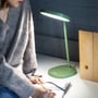 Kvinde sidder ved et skrivebord med grøn Lumie Task lampe tændt og skriver i en notesbog.