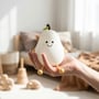 En hånd holder den hvide MOCHI pæreformede natlampe i blød silikone uden lys i et lyst rum.
