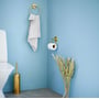 Smedbo Villa WC-børste i messing, vist ved siden af et toilet og messing badeværelsesudstyr på lyseblå væg.