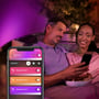 Et par styrer Philips Hue Resonate udendørs væglampe via appen, mens lilla lys skaber stemning omkring dem.