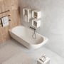Ideavit Solidnova badekar i hvid solid surface, 180x80 cm, med overløb og monteret op ad en grå betonvæg.