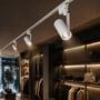 Flere hvide V-TAC 30 W CCT-skinnespots monteret på en skinne og belyst i en tøjbutik.