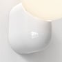 Detalje af Astro Lyra Wall Single væglampens blanke, hvide porcelænsbeslag og den runde, lysende skærm.