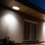 V-TAC LED-loftslampe med sort kant monteret under et udhæng og tændt, så den oplyser væggen.