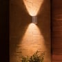 Philips Hue Resonate udendørs væglampe er monteret på en stenvæg og lyser varmt både opad og nedad.