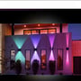Moderne husfacade med flere LEDlife Cubic væglamper, der skaber stemningsfuldt lys i grønne, lilla og pink farver om aftenen.