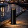 Light By Juul Platin-pullert lyser varmt på en træbro ved vandet i mørke.