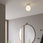 Astro Lighting Lyra loftlampe monteret i loftet over et rundt spejl, med den hvide skærm tændt.