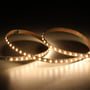 Ansell Lighting K-Cell LED strip på 50 meter med 4000K neutral hvidt lys, vist i en buet form på en mørk baggrund.