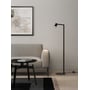 Astro Lighting Ascoli Floor gulvlampe i mat sort står ved en sofa i stuen med lampehovedet rettet nedad og lyset tændt.