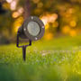 Sort V-TAC Pro havelampe med spyd placeret i en grøn have med bokeh baggrund.