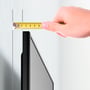 En hånd måler med et målebånd afstanden fra en væg til et fladt tv, hvilket illustrerer den tynde profil af et vægbeslag.