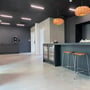 PureLED-lysskinner lyser i det mørke Troldtekt-loft over en bar med orange pendellamper.