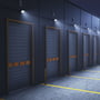 SpectrumLED Noctis Lux 4 projektører monteret ved lagerbygning, lyser op en række garageporte med varm hvidt lys.