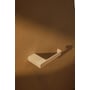 Metallbude Tuali toiletrulleholder i creamfarvet metal, vist på en brunlig væg med skygger.