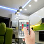 Modern stue med V-TAC RF-fjernbetjening der styrer blå LED-lys over sofaen og hvide spots i loftet.