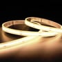 Ansell Lighting C-Cell COB LED strip, 50 meter rulle med 3000K varmt hvidt lys og 24V spænding, vist i varmt lys på mørk overflade.
