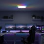 CCT loftlampe med RGBIC backlight, Ø30cm, oplyser et moderne gamer-rum med farverig belysning.