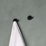 To mat sorte Cosmic håndklædekroge på en grå væg, hvorpå en hvid frottéhåndklæde hænger på den ene.