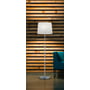 TRIO Lighting Lyon gulvlampe i børstet stål med hvid skærm, placeret foran en trævæg og ved siden af en blå sofa.