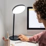Mand med krøllet hår bruger Lumie Task lysterapilampen ved et skrivebord foran en computer, mens han arbejder.