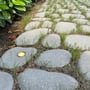Light By Juul indbygningsspot Cosmos i messing er tændt og lyser varmt hvidt ned i en stenbelagt havegang.