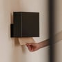 HeFe VILNIUS papirdispenser i matsort, vist på en væg med en hånd, der trækker et stykke papir ud.