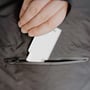 En hånd lægger den hvide Deltaco USB-C-vægoplader på 67 W ned i en mørk lomme.