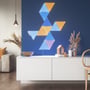 Nanoleaf Shapes Triangles monteret på en mørkeblå væg med et arrangement af lyseblå, orange og lyserøde paneler i en stue.