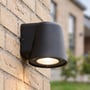 LEDlife Avero GU10-væglampe lyser nedad fra en murstensvæg, set skråt nedefra.
