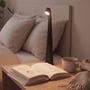 Den sorte genopladelige LED-bordlampe lyser ved sengen med varmt lys over en bog og en kop.