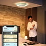 Philips Hue Being loftslampe er monteret i loftet, mens en person styrer lyset i Hue-appen på sin telefon.