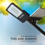 V-TAC LED solcelle gadelampe med teksten 'Zero electricity cost' og 'Fully solar powered', vist udendørs med et sløret grønt og blåt baggrundsbillede.