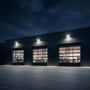 Tre V-TAC LED-projektører lyser facaden og indkørslen ved en lagerbygning om aftenen.