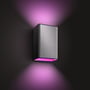 Philips Hue Resonate udendørs væglampe i børstet aluminium lyser lilla ned på den mørke væg.