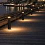 Flere Light By Juul Platin-pullertlamper lyser langs en træbro ved vandet om aftenen.