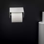 Fron view af Cosmic toiletpapirholder i mat hvid med låg, monteret på sort væg, klar til brug med en rulle toiletpapir.