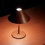 Halo Design Hygge bordlampe i mørkerød farve, tændt og placeret på et rødfarvet bord.