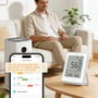 Sonoff AirGuard CO2-måleren står på et bord ved siden af en telefon, der viser CO2-, temperatur- og fugtdata.