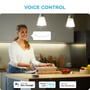 Kvinde i køkken bruger stemmestyring til at betjene WiZ lys, med ikoner for Hey Google, Alexa og Siri Shortcuts.
