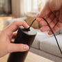 Hænder fastgør wiren til ophænget på den sorte, dæmpbare spisebordslampe med LED-lys.