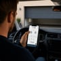 Zafe smart relay vises i brug, mens en bilist styrer garageporten fra Zafe-appen på sin telefon.