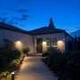 Light By Juul Platin slim pullerter lyser op langs flisegangen foran et hus om aftenen.