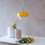 Dyberg Larsen HAIPOT pendel i gul, monteret over et bord med gul blomsterdekoration og lysegrå vase.